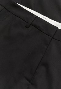 Czarne, dopasowane spodnie o gładkiej fakturze, prostych nogawkach i dyskretnych bocznych kieszeniach. Widoczna biała podszewka paska w talii.