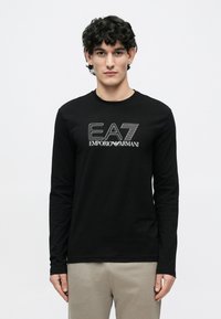 Must pikkade varrukatega T-särk pehmest kangast, ümar kaelus. Esiküljel valge graafiline logo "EA7 EMPORIO ARMANI".