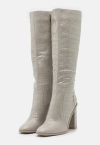Bottes stiletto montantes en gris clair avec un motif crocodile texturé, des panneaux lisses et un talon large pour plus de stabilité.