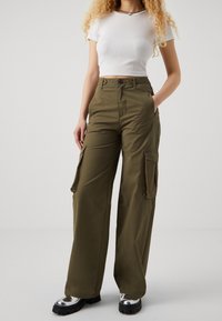 Olivgrön cargobyxor med avslappnad passform, med sidofickor och blixtlås, ihopparat med en figurnära vit ribbad crop top.