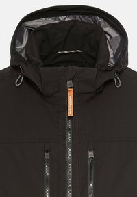 Veste noire avec capuche, dotée d'un intérieur doublé. Elle possède une fermeture à glissière à l'avant et deux poches zippées, avec un détail de tag brun.