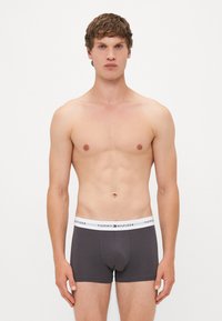 Szürke boxer alsónadrág fehér rugalmas derékkal, amelyen a "TOMMY HILFIGER" logó található. Sima anyag és testhez álló kialakítás. Nincs más figyelemre méltó részlet.