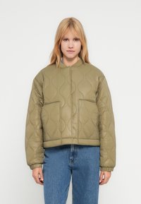 Πράσινο χακί μπουφάν με καπιτονέ ύφασμα, κοντό σχέδιο, στρογγυλή λαιμόκοψη και δύο μπροστινές τσέπες. Μαλακή υφή με διακριτικά κυματιστά μοτίβα.