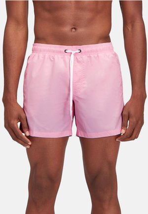 Uomo che indossa pantaloncini da bagno rosa chiaro con cordoncino bianco, mostrato dal torso fino a metà coscia su uno sfondo bianco semplice.