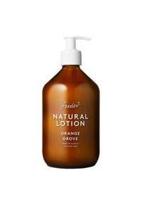 Bottiglia di vetro ambra con pompa bianca etichettata "soeder Natural Lotion Orange Grove", prodotta a Zurigo, Svizzera, su sfondo bianco.