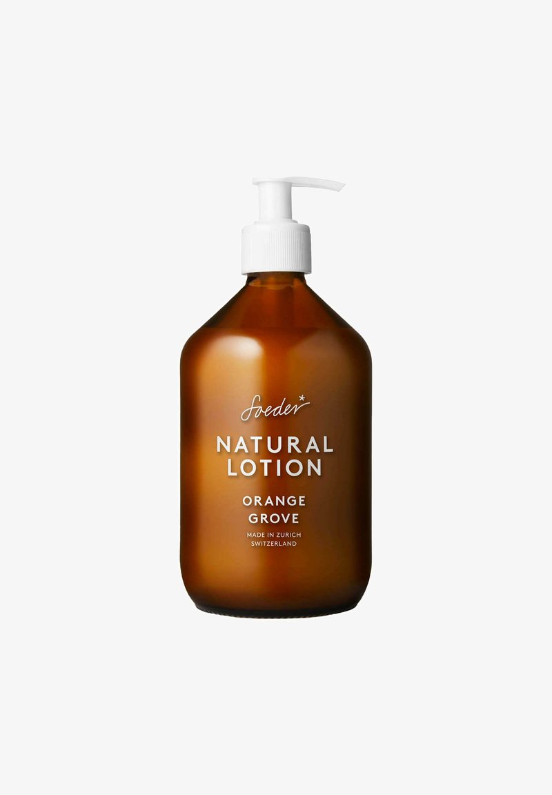 Bottiglia di vetro ambra con pompa bianca etichettata "soeder Natural Lotion Orange Grove", prodotta a Zurigo, Svizzera, su sfondo bianco.