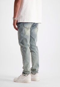 Lichtblauwe denim jeans met een ontspannen pasvorm, met een vervaagde uitstraling en achterzakken. Draagt samen met witte sneakers.