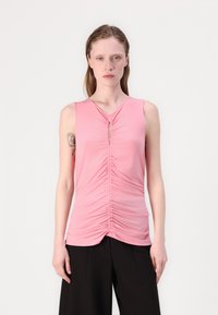 Rosa ärmlös topp med samlad textur och en nyckelhålsgym vid halsringningen. Mjuk tyg med en figurnära silhuett.