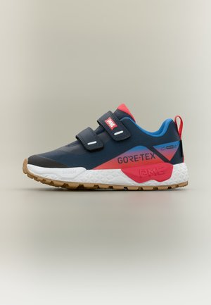 Baskets Gore-Tex bleues et rouges avec semelle blanche, deux bandes Velcro noires et semelle extérieure marron crantée, vues de côté sur fond beige.