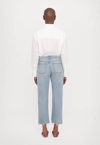 Camicia bianca a maniche lunghe e jeans a vita alta blu chiaro con orli sfilacciati, cinque tasche e dettagli di cucitura sottili.