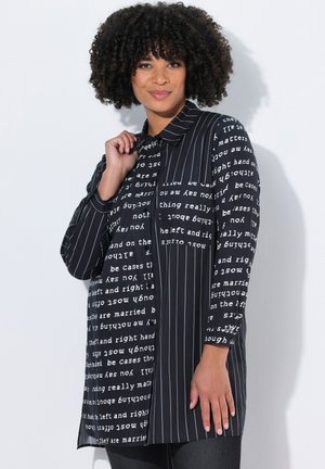 Camisa de botones negra con una combinación de texto y patrones a rayas. Presenta mangas largas y un cuello puntiagudo. Textura de tela suave.