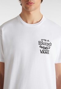 Witte katoenen t-shirt met een zwart grafisch ontwerp met de tekst "IT'S A Warped WORLD VANS" op de bovenste linkerzijde. Korte mouwen, ronde hals.