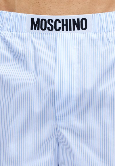 Υφασμα με λεπτές ρίγες σε ανοιχτό μπλε και άσπρο, με λευκή ζώνη μέσης που φέρει έντονα μαύρα γράμματα "MOSCHINO".