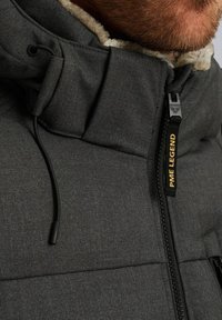 Siv puffer jakna z dvignjenim ovratnikom z umetnim krznom, črnimi zadrgami in oznako blagovne znamke "PME LEGEND." Teksturna tkanina.