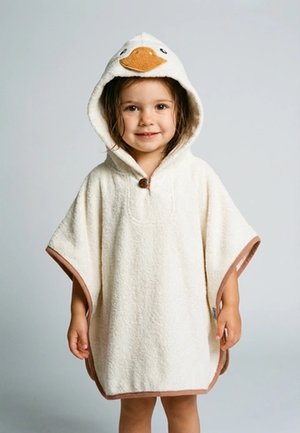 Junges Kind lächelt, trägt ein weißes Kapuzenhandtuch-Poncho mit Entengesicht und Schnabel-Design auf der Kapuze.