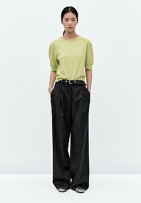 Maglione verde chiaro a maniche corte abbinato a pantaloni neri a vita alta e gamba larga, con scarpe argentate. L'outfit ha una vestibilità rilassata.