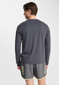 Grå långärmad skjorta med kontrasterande gula sömmar, parat med grå shorts med gula inslag ochChevron-mönster.