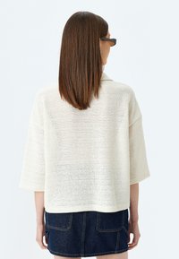 Strikket, lys creme sweater med løs pasform, sænkede skuldre og ærmer til albuen. Tekstureret stof og ribbet kant. Båret med en mørk denimnederdel.