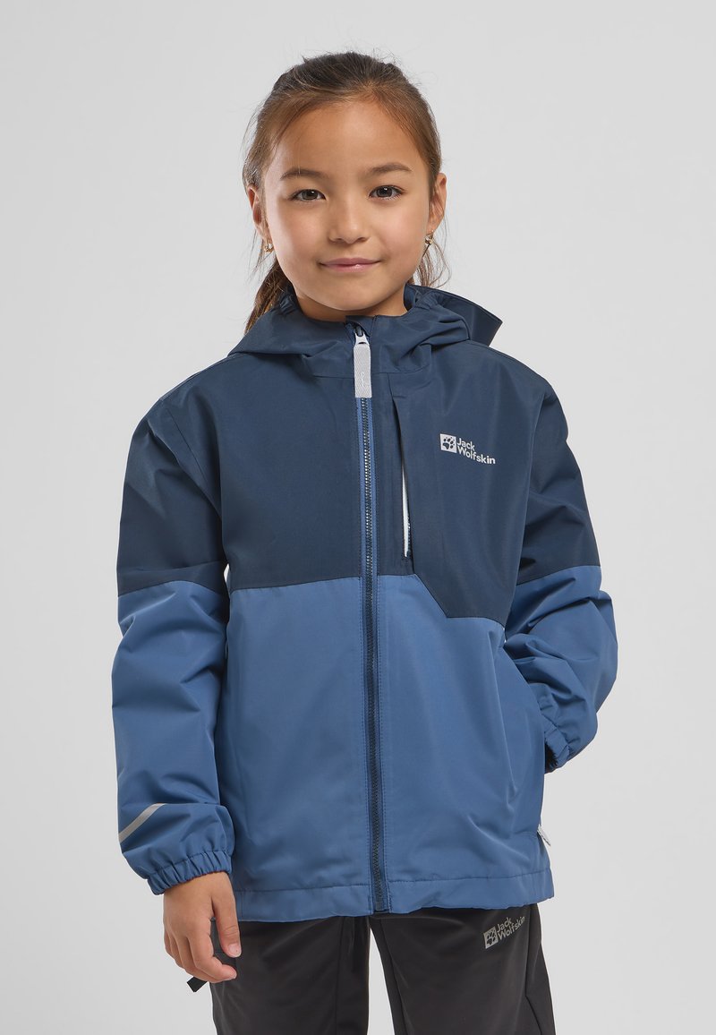 Blauwe waterdichte jas met capuchon, contrasterend donkerblauw bovenstuk, elastische manchetten en reflecterende accenten. Logo op de borst.
