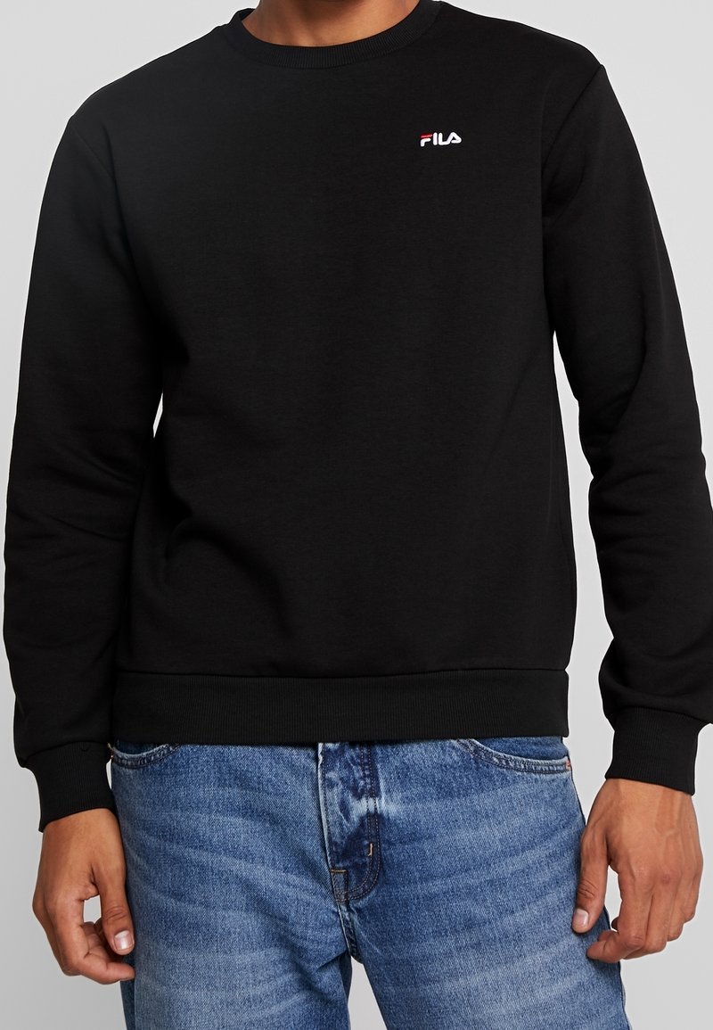Black crewneck sweatshirt made from cotton blend, featuring a small white logo on the chest, and ribbed cuffs and hem.
