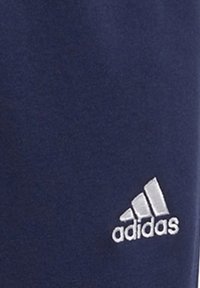 Navy blå treningsbukser laget av myk stoff har et hvitt Adidas-logo på nedre venstre ben, med en glatt tekstur og tettsittende design.