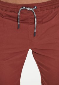 Rostfärgade shorts i mjukt tyg, med ett marinblått och vitt flätat snöre. Slät yta med elastisk midja.