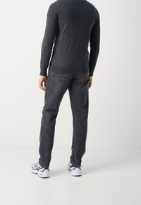 Maglione grigio scuro con scollatura rotonda e maniche lunghe, abbinato a jeans neri sbiaditi e sneaker bianche con dettagli grigi.