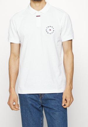 Biała koszulka polo wykonana z bawełny, z kołnierzykiem, krótkimi rękawami i okrągłym logo w granatowym kolorze z czerwonymi i białymi akcentami na klatce piersiowej.