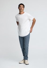 Camiseta blanca de manga corta combinada con pantalones azul claro. El conjunto se completa con zapatillas beige con detalles y cordones negros.