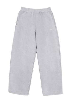 Person trägt hellgraue, weit geschnittene Jogginghosen und beige Arbeitsschuhe, steht mit den Händen in den Taschen des Kapuzenpullovers.