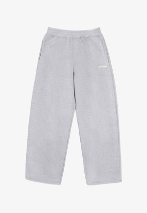 Persoon die lichtgrijze wijde sweatpants en beige werkschoenen draagt, staand met handen in de zakken van de hoodie.