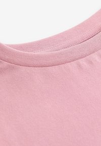 Tricou roz din bumbac cu guler rotund și textură netedă. Materialul pare moale și ușor, având un design simplu.