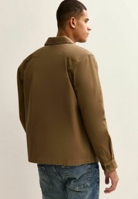 Bruin, langemouw hemd met een zachte textuur en knoopmanchetten. Heeft een klassieke kraag en een rechte snit, gedragen over blauwe jeans.