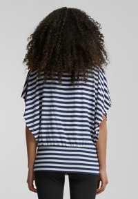 Haut rayé présentant des couleurs bleu marine et blanches, coupe ample, manches chauve-souris courtes et un ourlet froncé à la taille. Le tissu semble doux et léger.