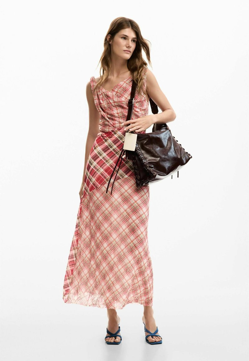 Sukienka maxi w różową kratę z dopasowanym gorsetem i zwiewną spódnicą; zestawiona z czarną skórzaną torebką i niebieskimi sandałami.
