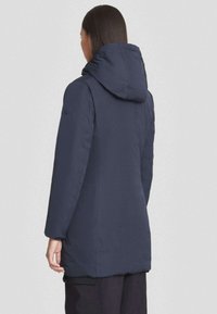 Marineblauwe pufferjas met een capuchon, voorzien van lange mouwen, een rechte snit en een gladde textuur, met zichtbare stiksels aan de zoom.