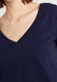Camiseta de pico azul marino con textura suave y lisa, de mangas cortas, con un diseño simple y sin patrones ni adornos visibles.