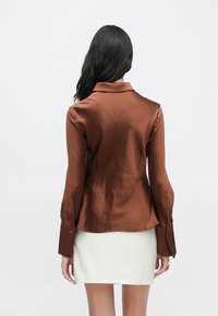 Braunes Satinschirt mit Kragen, langen Ärmeln und knöpfbaren Manschetten, mit strukturierter Oberfläche und tailliertem Schnitt.