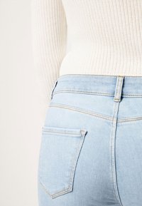 Ljusblå denimjeans med en slät yta, med en bakficka och kontrastsöm, bärs med en vit ribbad tröja.