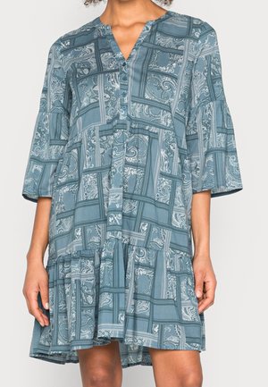 Sukienka w kolorze morskim z dekoltem w serek, zapinana z przodu na guziki, z rękawami do połowy przedramienia. Charakteryzuje się wzorzystym wzorem i warstwową falbaną u dołu.