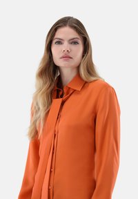 Orange long-sleeve blouse with a collar, featuring a button-down front and smooth texture. Fabric appears lightweight and slightly glossy.