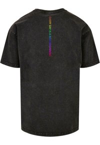 T-shirt noir à manches courtes avec une texture douce. Présente un texte coloré à l'arrière disant "CHAQUE JOUR EST UN NOUVEAU DÉPART" en couleurs arc-en-ciel.