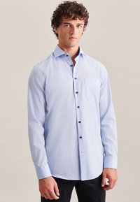 Lichtblauw overhemd met lange mouwen, knopen en een borstzak, zwarte knopen, gewone kraag en een gladde textuur. Draagt donkergekleurde broek.