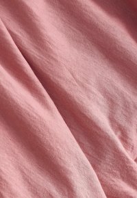 Tissu rose doux avec de subtiles rides et plis, montrant une texture fine en maille et une ombre douce.