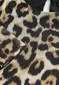 Tissu à motif léopard avec un mélange de couleurs beige, noir et marron. Présente une texture lisse avec des taches distinctes et des coutures soignées.
