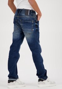 Jeans de mezclilla azul oscuro con un ligero desgaste, estilo de cinco bolsillos con detalles de costura y una etiqueta negra en la cinturilla trasera.