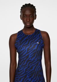 Bezrękawnik sportowy w niebiesko-czarny wzór w paski tygrysa; gładki materiał z okrągłym dekoltem i małym białym logo na klatce piersiowej.