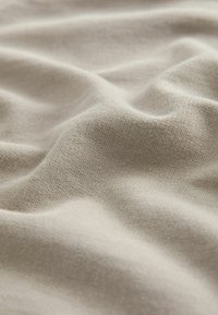 Tessuto beige con una superficie morbida e testurizzata, caratterizzato da leggere pieghe e arricciature, che evidenziano la sua elasticità e leggerezza.