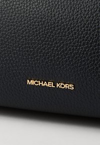 Black pebbled leather bag featuring a gold "Michael Kors" logo. The texture is textured with a subtle pattern, adding depth to the design.