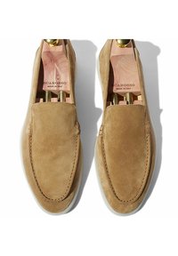 Scarpe slip-on in suede beige con suole in gomma bianca, caratterizzate da cuciture visibili e forme interne in legno, logo del marchio impresso sulla soletta.
